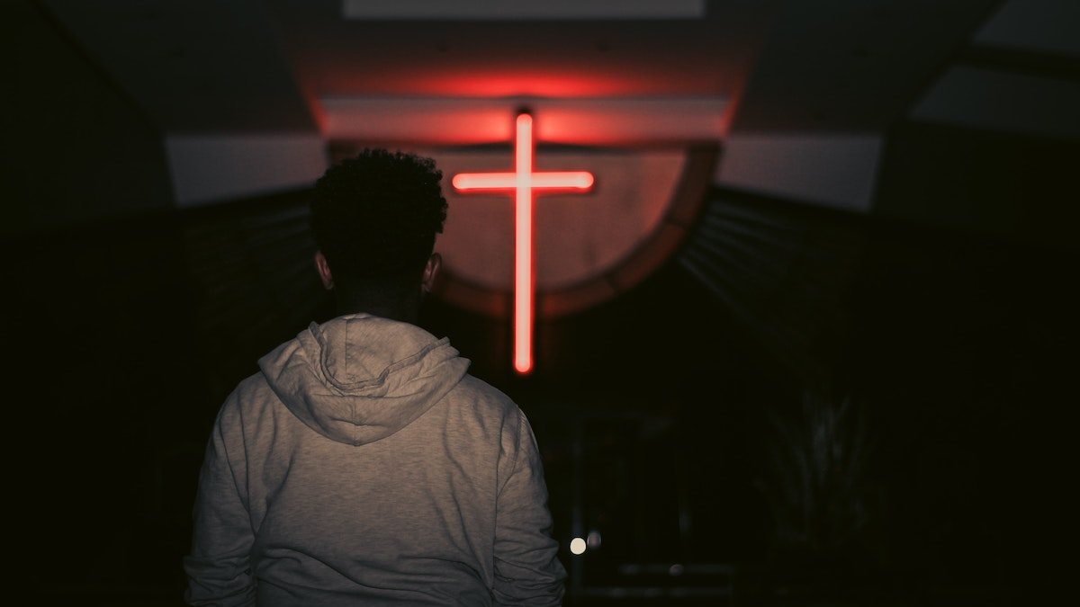 young man looks at red neon cross