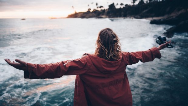 a girl with her arms outstretched stands on the beach and looks at the sea