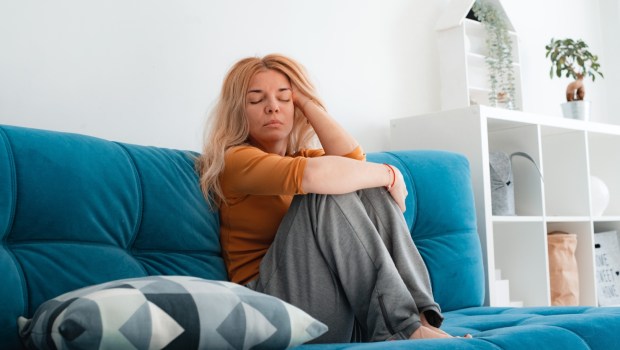 nieszczęśliwa kobieta siedzi na kanapie z podkurczonymi nogami