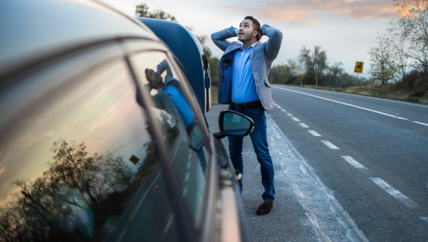 Zmartwiony mężczyzna stoi przy zepsutym samochodzie