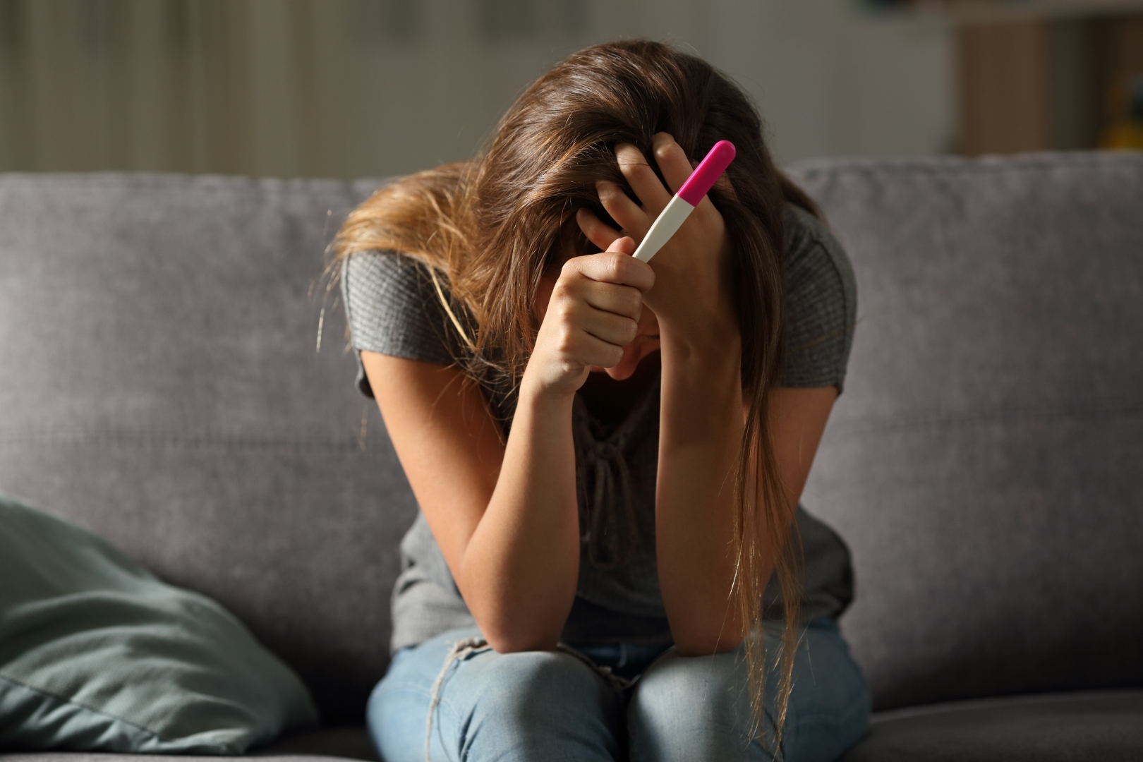 Smutna dziewczyna siedzi sama na kanapie trzymając w dłoni test ciążowy