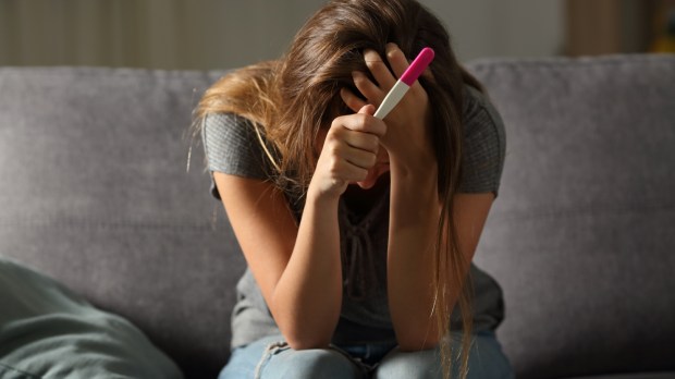 Smutna dziewczyna siedzi sama na kanapie trzymając w dłoni test ciążowy
