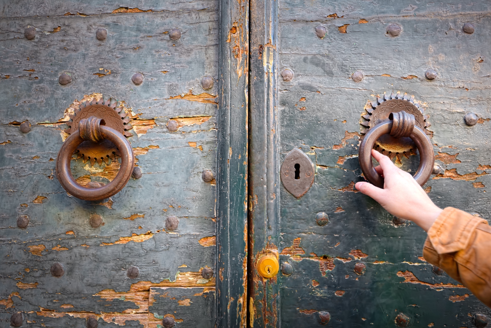 kobieca dłoń trzyma kołatkę przy starych drzwiach