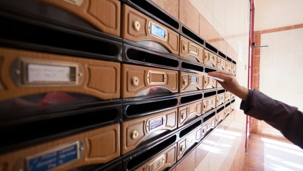 kobieca ręka wkłada list do jednej ze skrzynek na listy w bloku