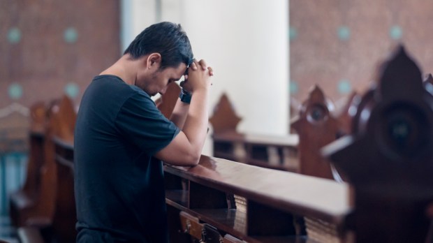 mężczyzna modli się samotnie w kościelnej ławce