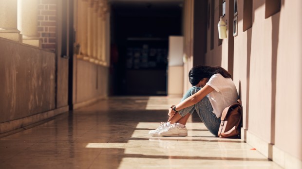 pogrążona w smutku młoda dziewczyna z liceum siedzi samotnie na szkolnym korytarzu i chowa głowę