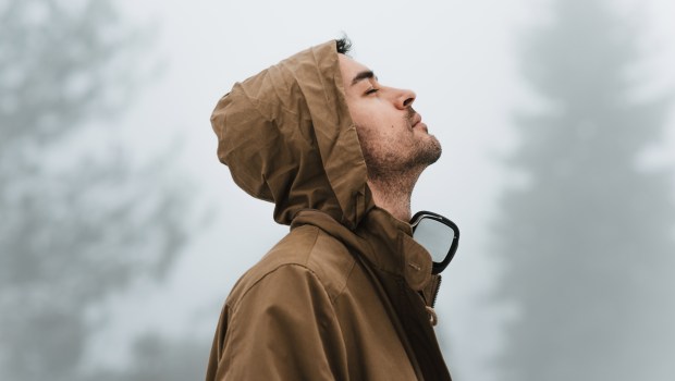 mężczyzna stoi w lesie i wyciąga głowę w górę z zamkniętymi oczami