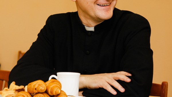 Ksiądz zaproszony do domu rozmawia przy stole z członkami rodziny