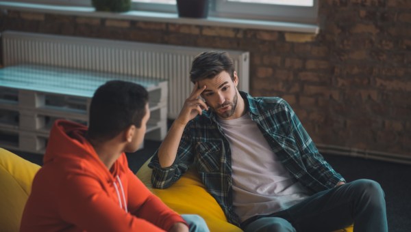 dwaj przyjaciele rozmawiają ze sobą siedząc na kanapie wewnątrz mieszkania