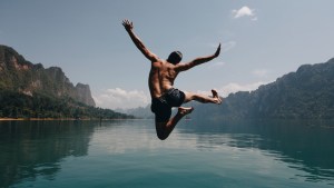 Mężczyzna skacze z radością do górskiego jeziora
