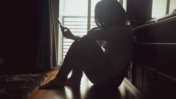 zdesperowana kobieta sięga po telefon, by zadzwonić po pomoc