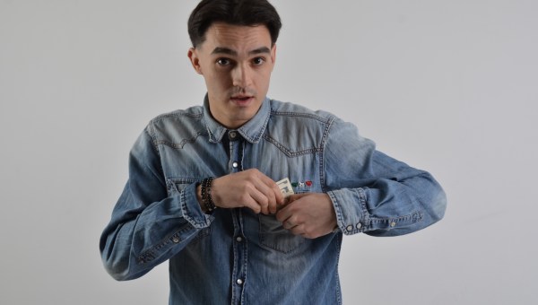 młody mężczyzna z zaskoczoną miną chowa pieniądze do kieszeni dżinsowej koszuli