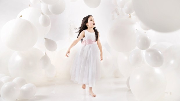 szczęśliwa mała dziewczynka w białej sukience wchodzi do pomieszczenia wypełnionego białymi balonami