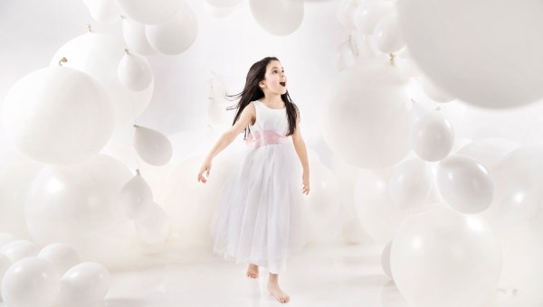 szczęśliwa mała dziewczynka w białej sukience wchodzi do pomieszczenia wypełnionego białymi balonami