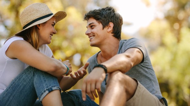 Para małżonków rozmawia ze sobą siedząc na trawie w parku w ciepły letni dzień