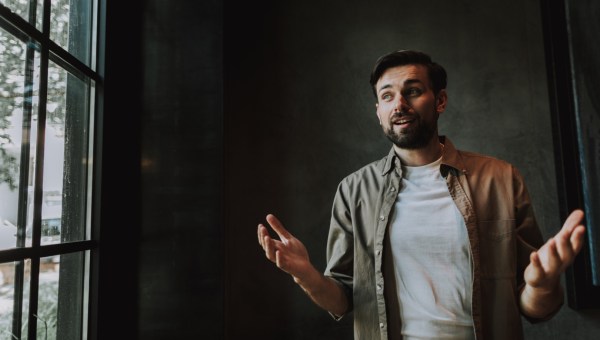 Mężczyzna w zaciemnionym pokoju szeroko gestykuluje rękami