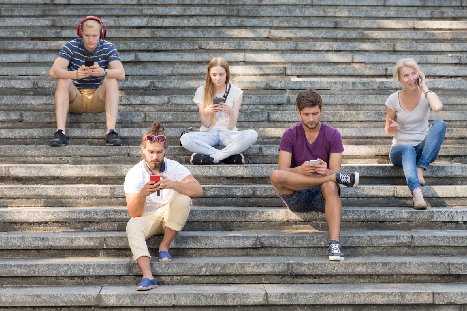 Pięcioro ludzi siedzi na dużych schodach w mieście i używa swoich telefonów