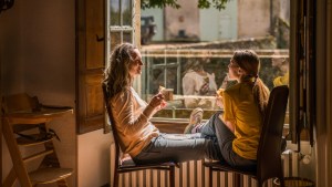 Matka z nastoletnią córką siedzą w mieszkaniu przy oknie i piją herbatę