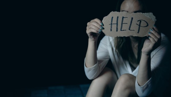 Scared and abused woman holding the paper with handwritten help sign
