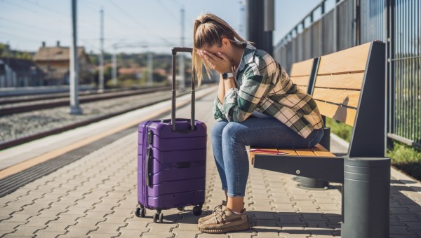 Stres przed urlopem: kobieta z walizką podróżną siedzi zmartwiona na ławce na stacji kolejowej