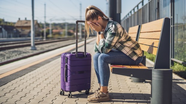Stres przed urlopem: kobieta z walizką podróżną siedzi zmartwiona na ławce na stacji kolejowej