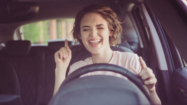 Kobieta prowadzi samochód słuchając głośno muzyki i kołysząc się w jej rytm