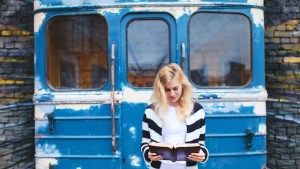 Młoda dziewczyna czyta Biblię stojąc przed starym i pomalowanym graffiti wagonem metra