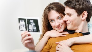 Kobieta i mężczyzna przytulają się do siebie i oglądają razem zdjęcie USG dziecka