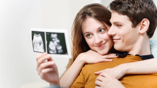 Kobieta i mężczyzna przytulają się do siebie i oglądają razem zdjęcie USG dziecka