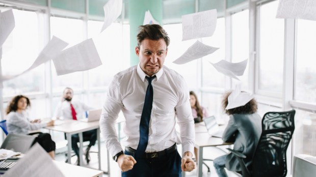 Wściekły menadżer rzuca papierami w biurze na oczach współpracowników