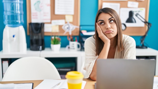 Stres powakacyjny: pracownica biura siedzi zmęczona za biurkiem i spogląda zamyślona w górę