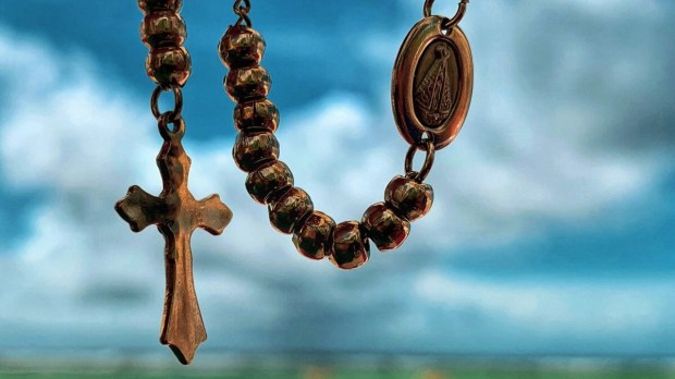 Close up of rosary against a cloudy sky and green grassy background