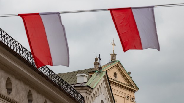 Biało-czerwone polskie flagi na pierwszym planie, w tle wieże kościołów