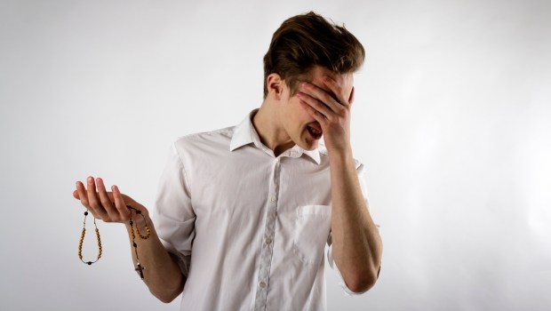 Młody mężczyzna z niechęcią podchodzi do modlitwy różańcowej