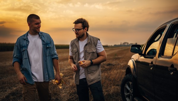 Dwóch mężczyzn rozmawia ze sobą na polu obok samochodu