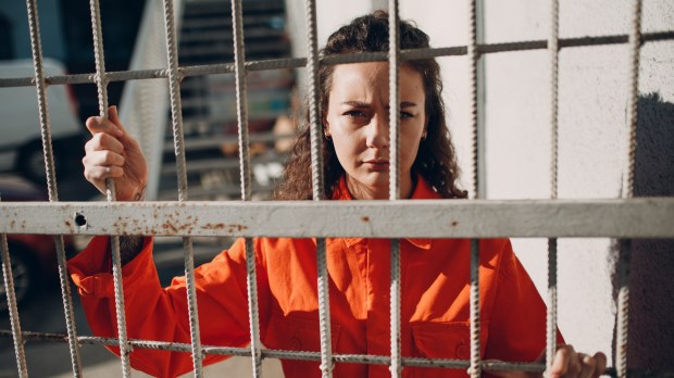 Kobieta w pomarańczowym uniformie więziennym stoi za kratkami