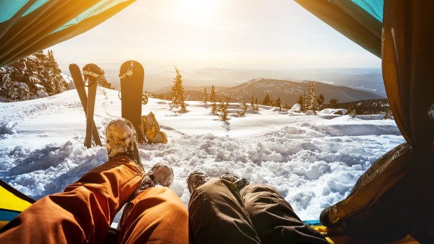 Para narciarzy odpoczywa w namiocie. Ich narty i snowboard leżą przed nimi wbite w śnieg