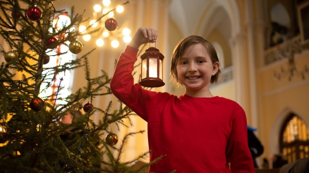 Dziewczynka z lampionem stoi przy choince w kościele