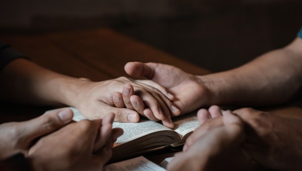 Grupa ludzi trzyma się za ręce i modli się przy Pismie Świętym