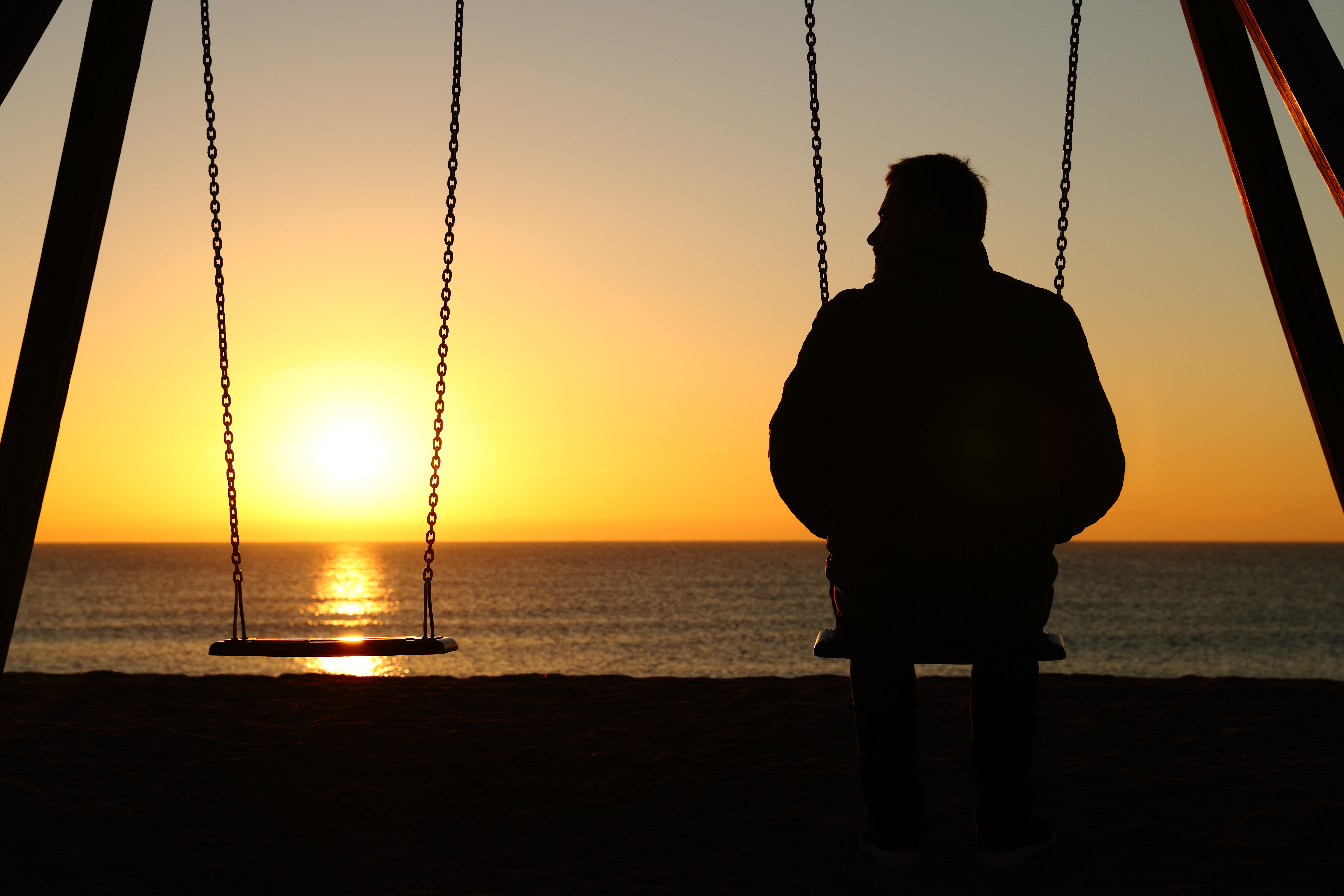 Samotny mężczyzna na huśtawce tęsknie patrzy na zachodzące słońce