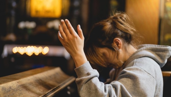 Kobieta klęczy w kościele i modli się z uniesionymi rękoma