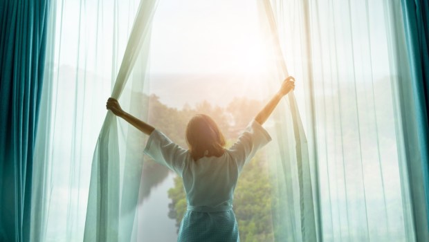 Kobieta rozsuwa zasłony w sypialni