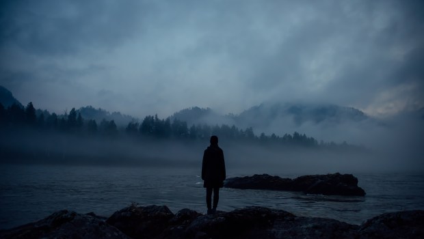 Osoba na ciemnym tle patrzy na zamglony krajobraz